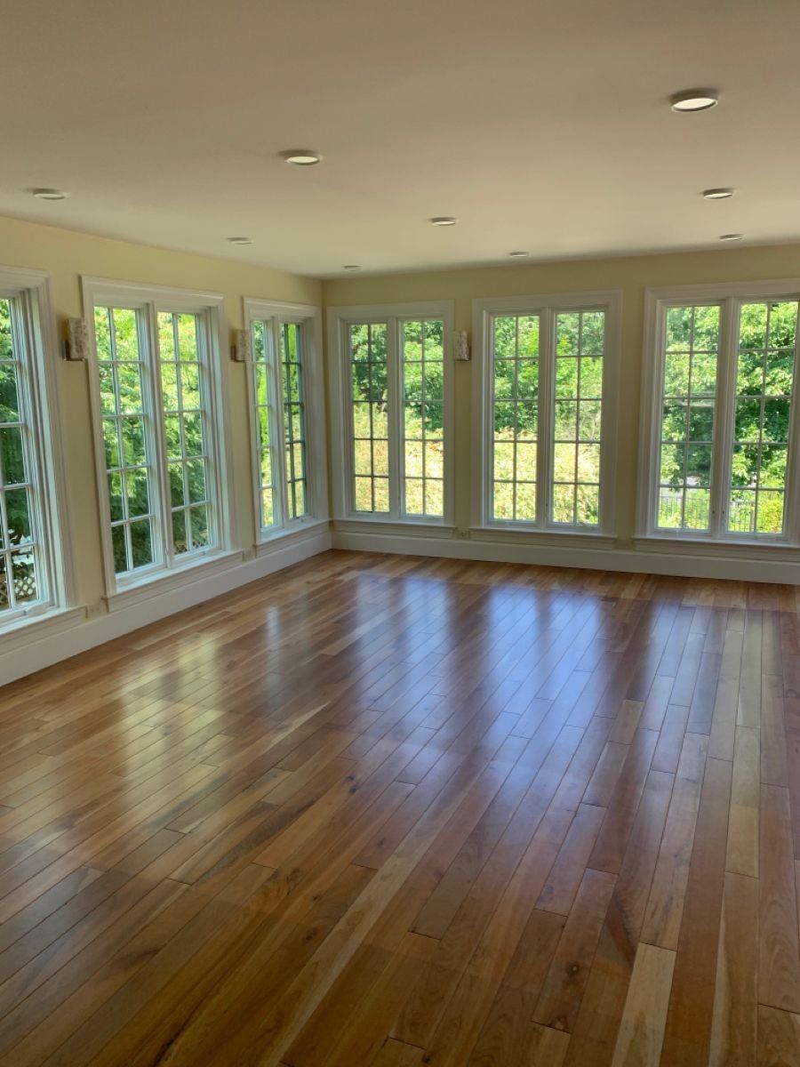 An empty, sunlit room after a move-out clean, with gleaming hardwood floors and a wall of windows