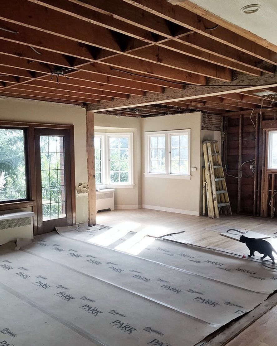 A home mid-remodel with open ceiling joists, protective floor paper and a ladder